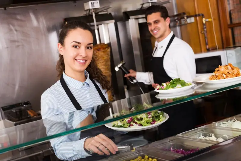 Two cheerful chefs serving fresh dishes at a restaurant counter.